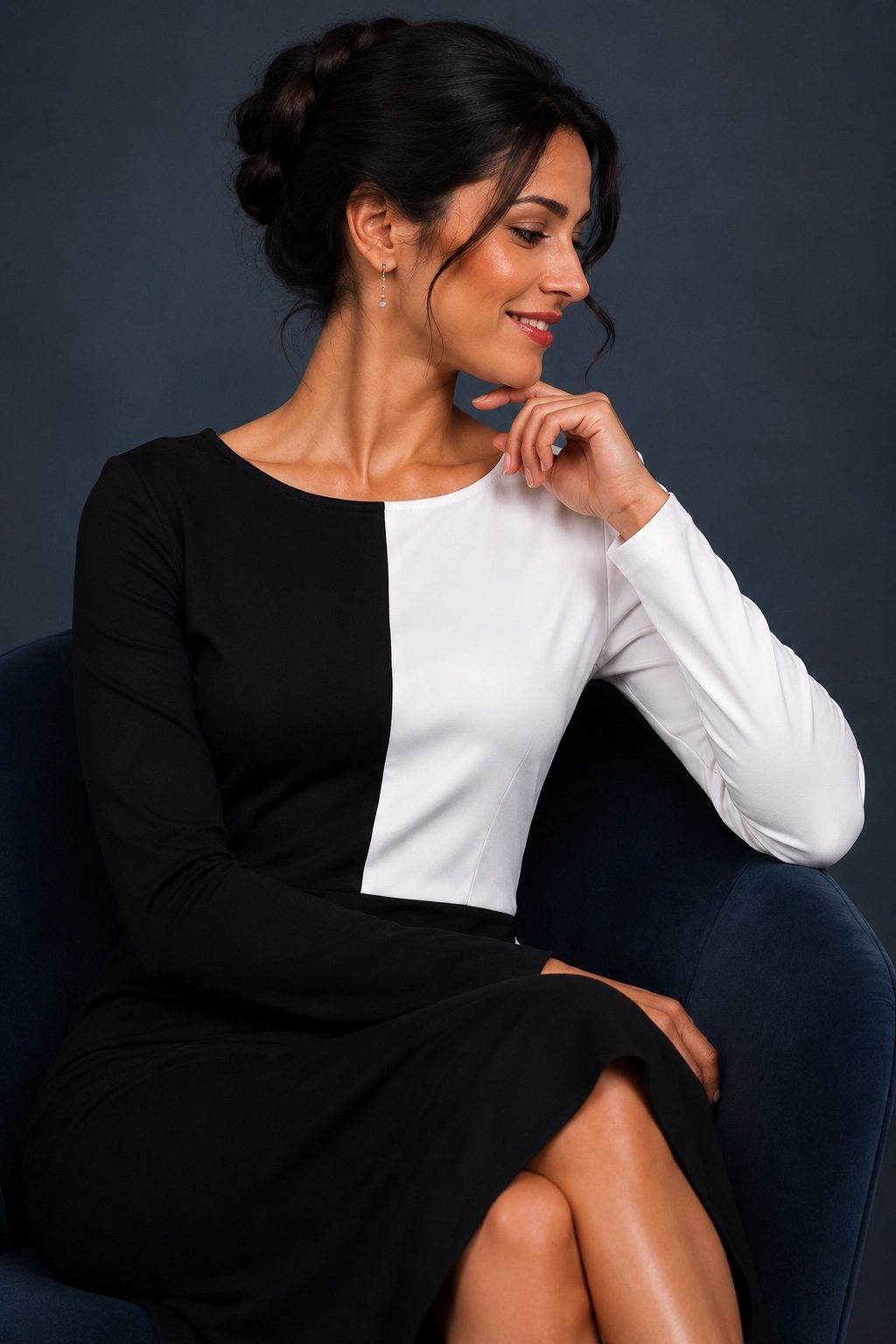 A woman wearing a long-sleeve colorblock pencil dress with a black and white split design, posed against a dark textured studio background.