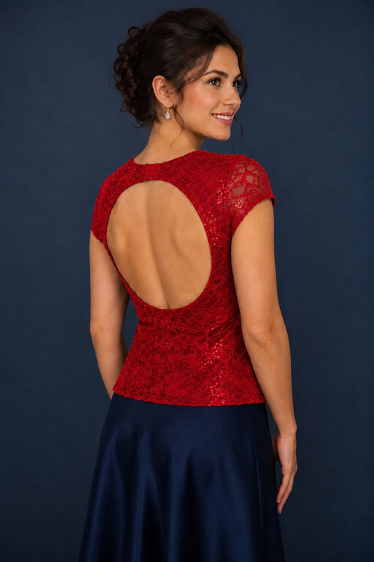 A woman shown from the back wearing a red lace dress with a large open back and short cap sleeves, paired with a navy satin skirt, against a dark blue studio background.