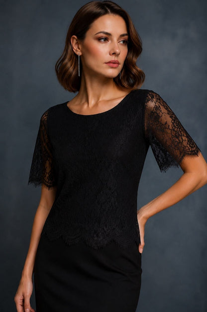 A woman modeling a black short-sleeve dress with sheer lace sleeves and a matching black skirt against a dark gray studio background.