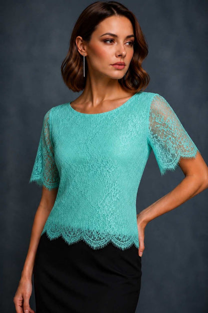 A woman modeling a turquoise lace short-sleeve top with a scalloped hem, paired with a black skirt, against a dark gray studio background.