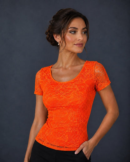 A woman modeling a bright neon orange short-sleeve lace top against a dark gray studio background.