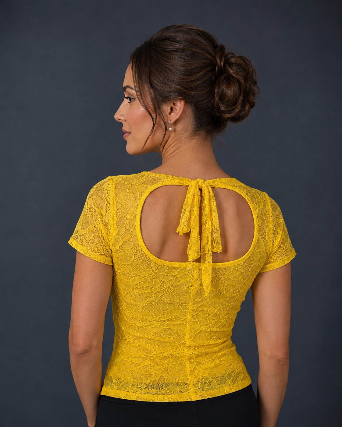 A woman shown from the back wearing a bright yellow lace short-sleeve top with a large open back and tie detail.