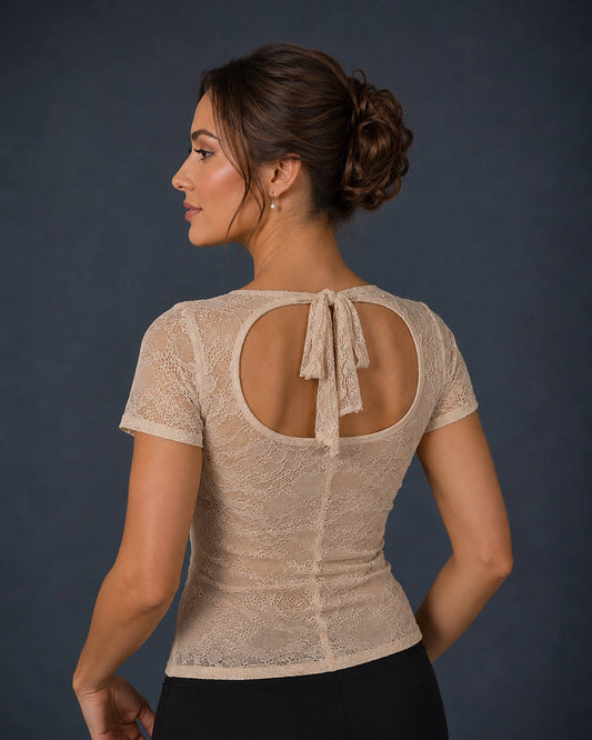 A woman shown from the back wearing a beige lace short-sleeve top with a large open back and tie detail, paired with black bottoms, against a dark gray studio background.
