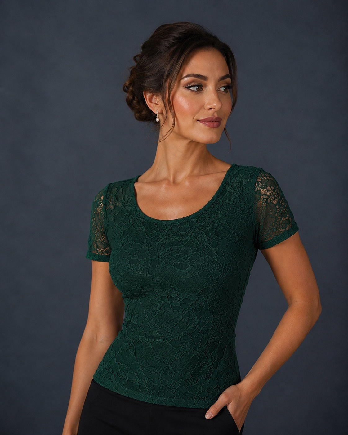 A woman wearing a dark green lace short-sleeve scoop-neck top, posed against a dark gray studio background.