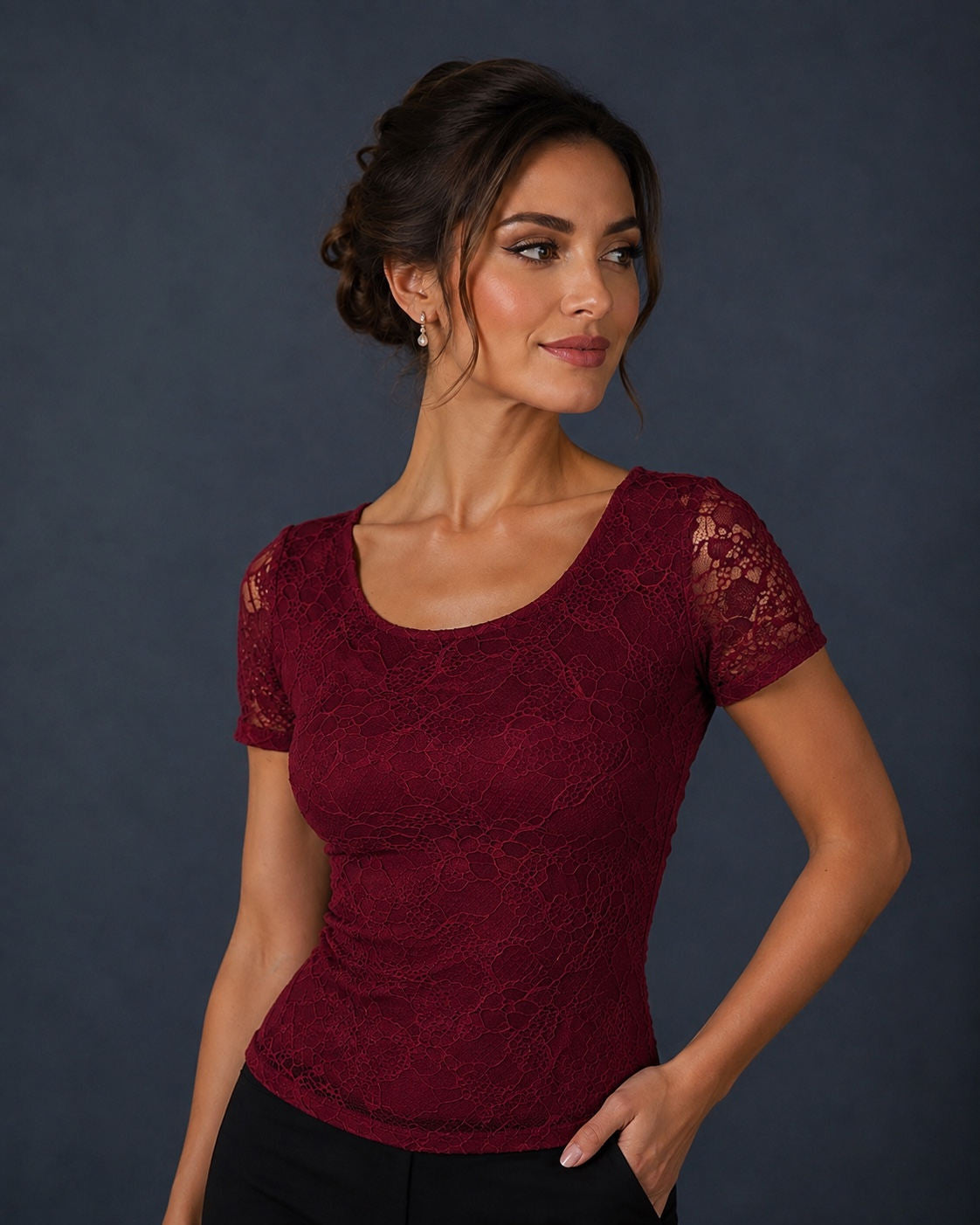 A woman wearing a short-sleeve burgundy lace top with sheer lace sleeves, posed against a dark slate gray studio background.