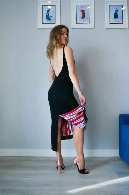 Woman in a black tango dress with a red and white striped hem in a room with framed pictures on the wall.
