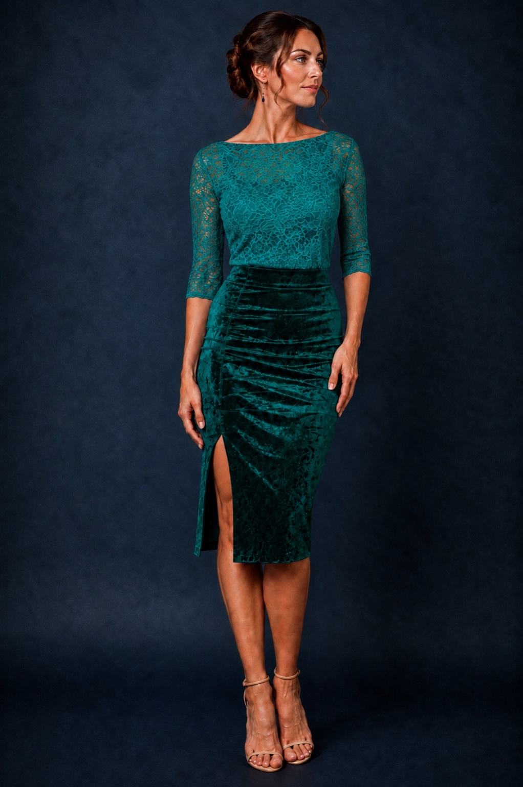 A woman models a dark teal green midi dress with a lace bodice, three-quarter sleeves, and a ruched velvet skirt with a side slit, set against a dark blue studio backdrop.