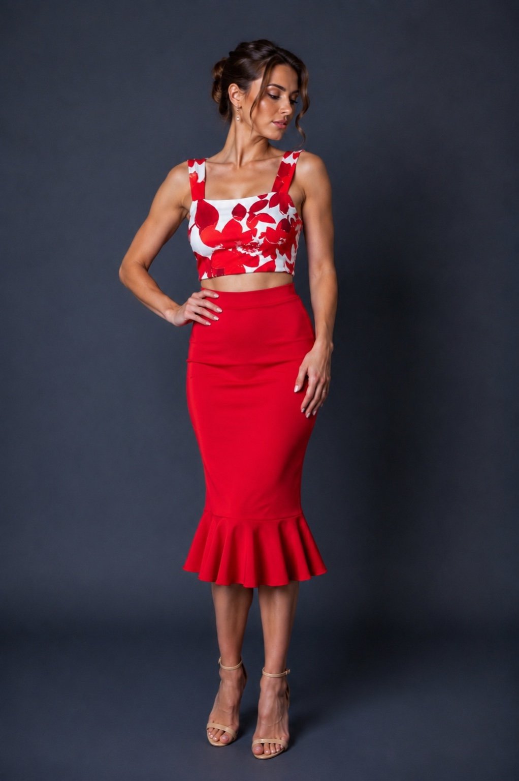 A woman modeling a two-piece red and white floral print set, featuring a sleeveless crop top and a high-waisted red flared midi skirt, against a dark gray studio background.