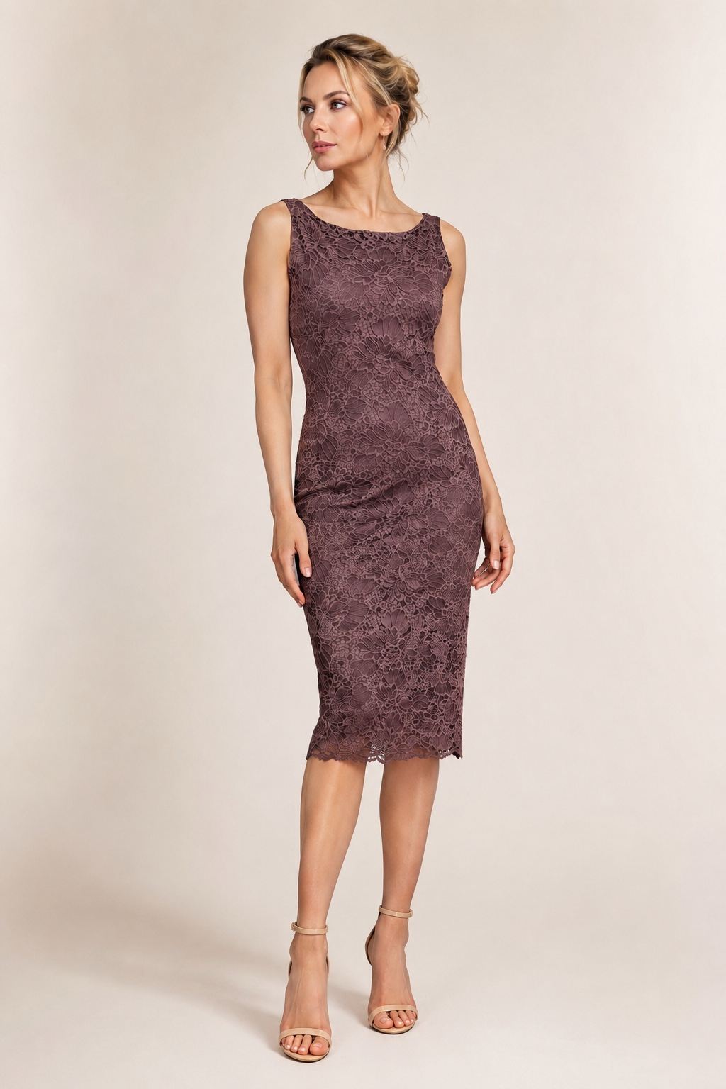 A woman modeling a sleeveless, knee-length lace dress in a muted plum-brown color, paired with beige high-heeled sandals, against a plain beige studio background.