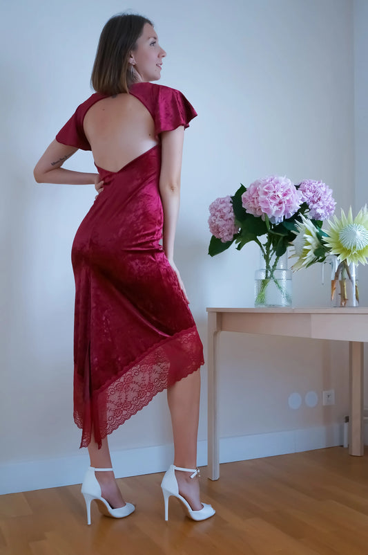 Woman in a red tango dress standing in a room with flowers on a table.