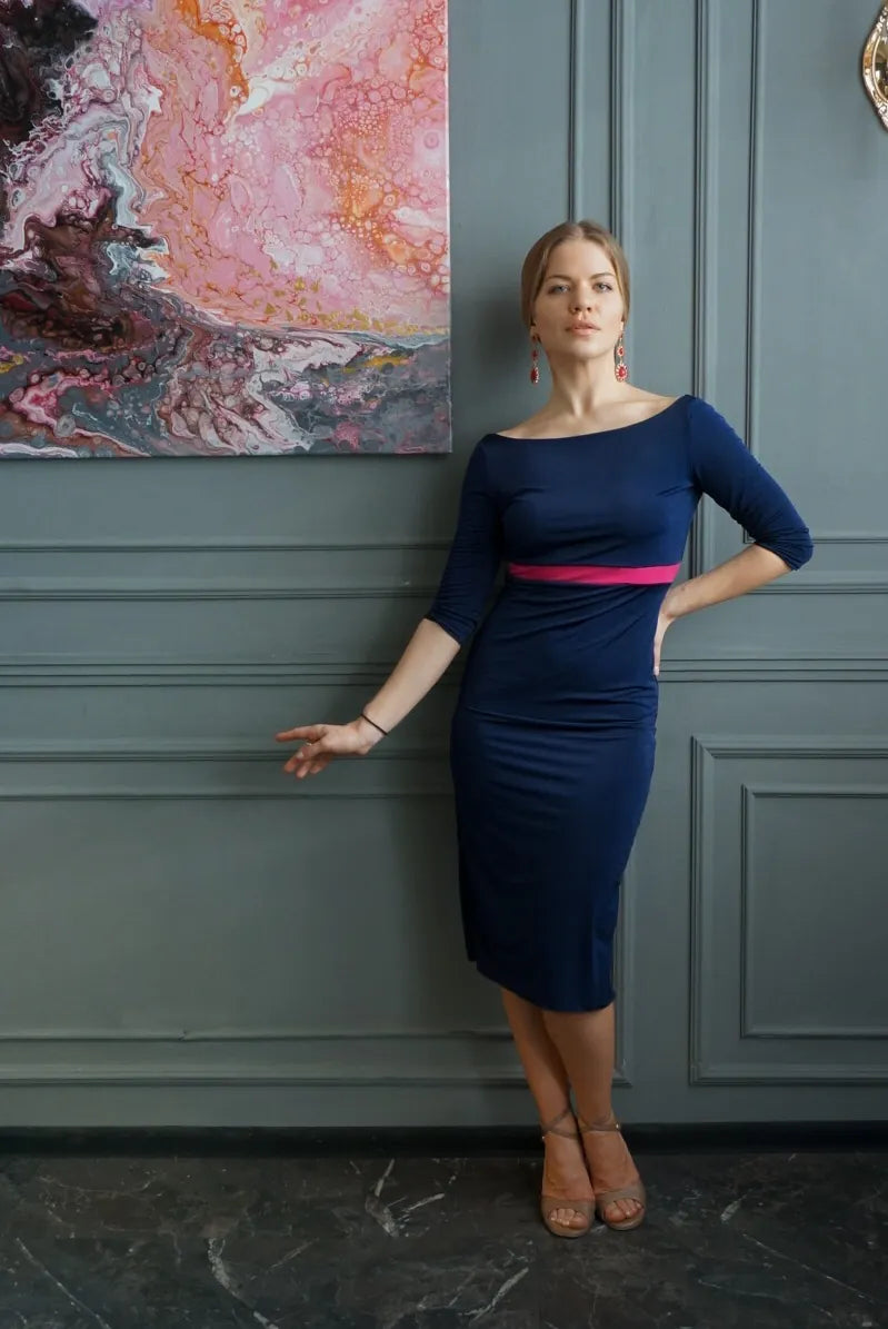 Woman in a blue tango dress elegantly standing against a gray wall.