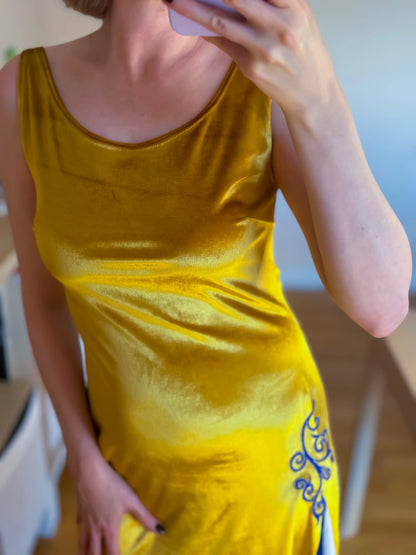 Woman wearing a golden velvet tango dress with blue patterns, standing indoors.