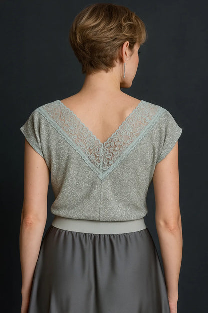 Woman wearing a silver shimmer tango top with lace detailing and a gray skirt against a black background, back view