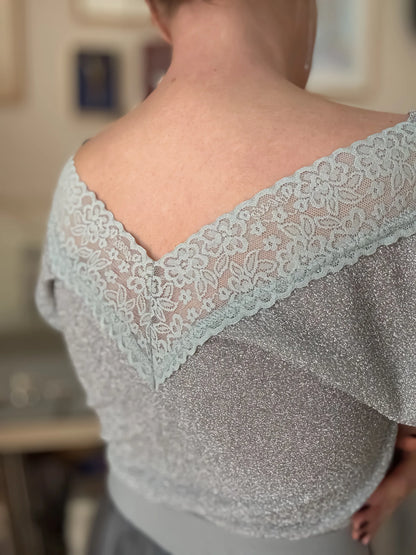 Woman wearing a silver shimmer tango top with a blurred background, back view
