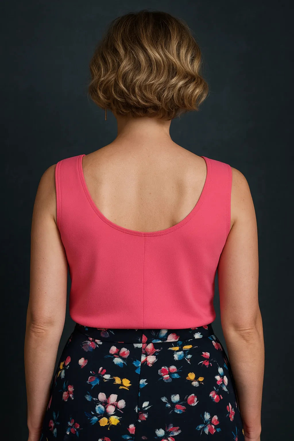 Woman wearing a pink tango top and floral skirt against a dark background, back view
