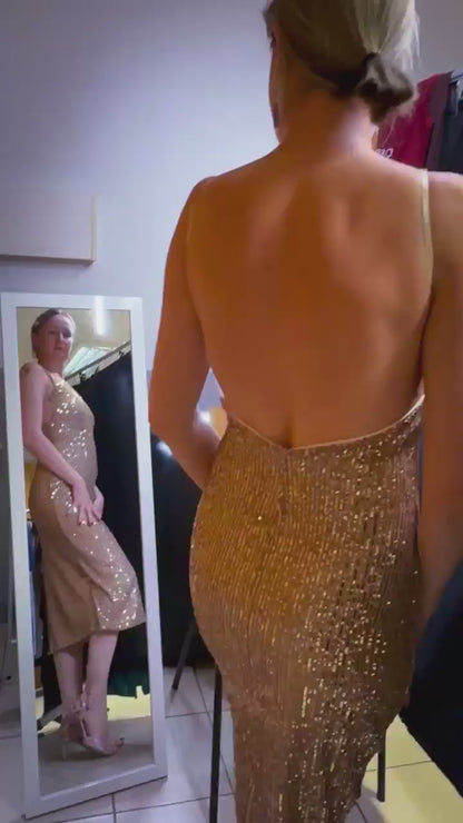 Woman wearing a golden sequin tango dress with open back in front of the mirror